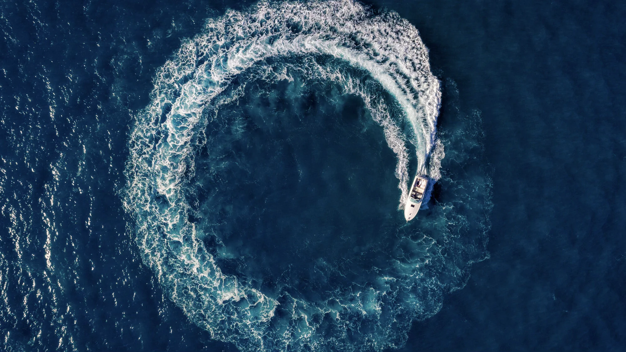 A speedboat tracing a circular wake across deep blue water